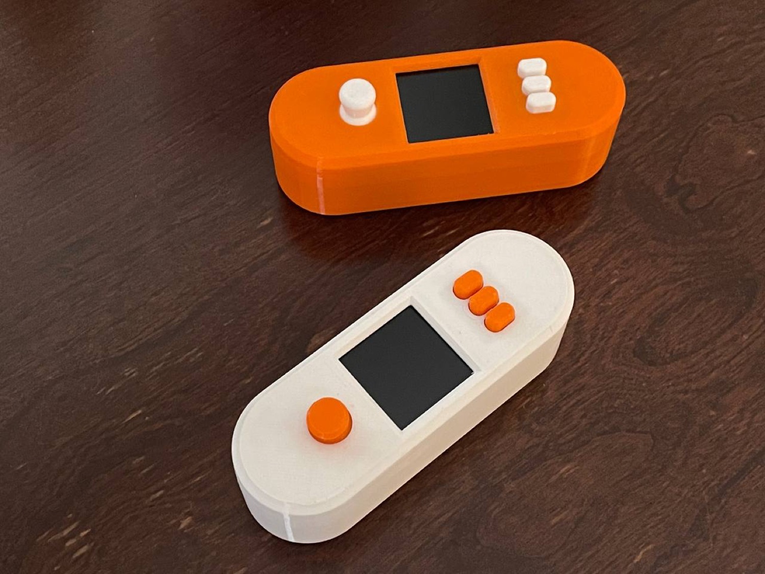 Two pill-shaped 3D printed SeedSigner enclosures, one orange with white buttons and one white with orange buttons